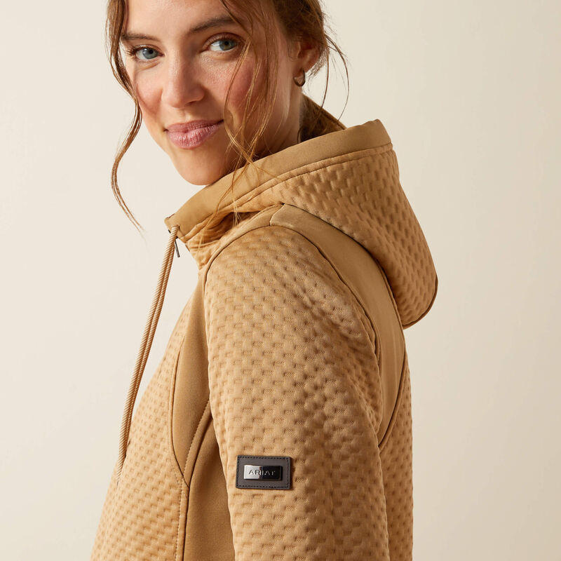 Woman wearing a beige quilted jacket with a brand logo on a beige background