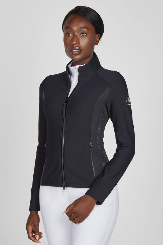 Model wearing a black functional jacket and white breeches on a plain background