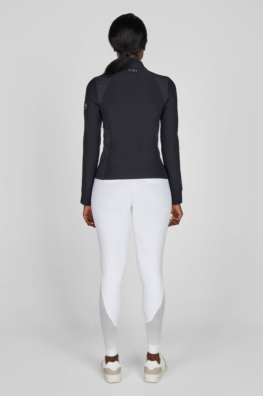 Model wearing a black functional jacket and white breeches on a plain background