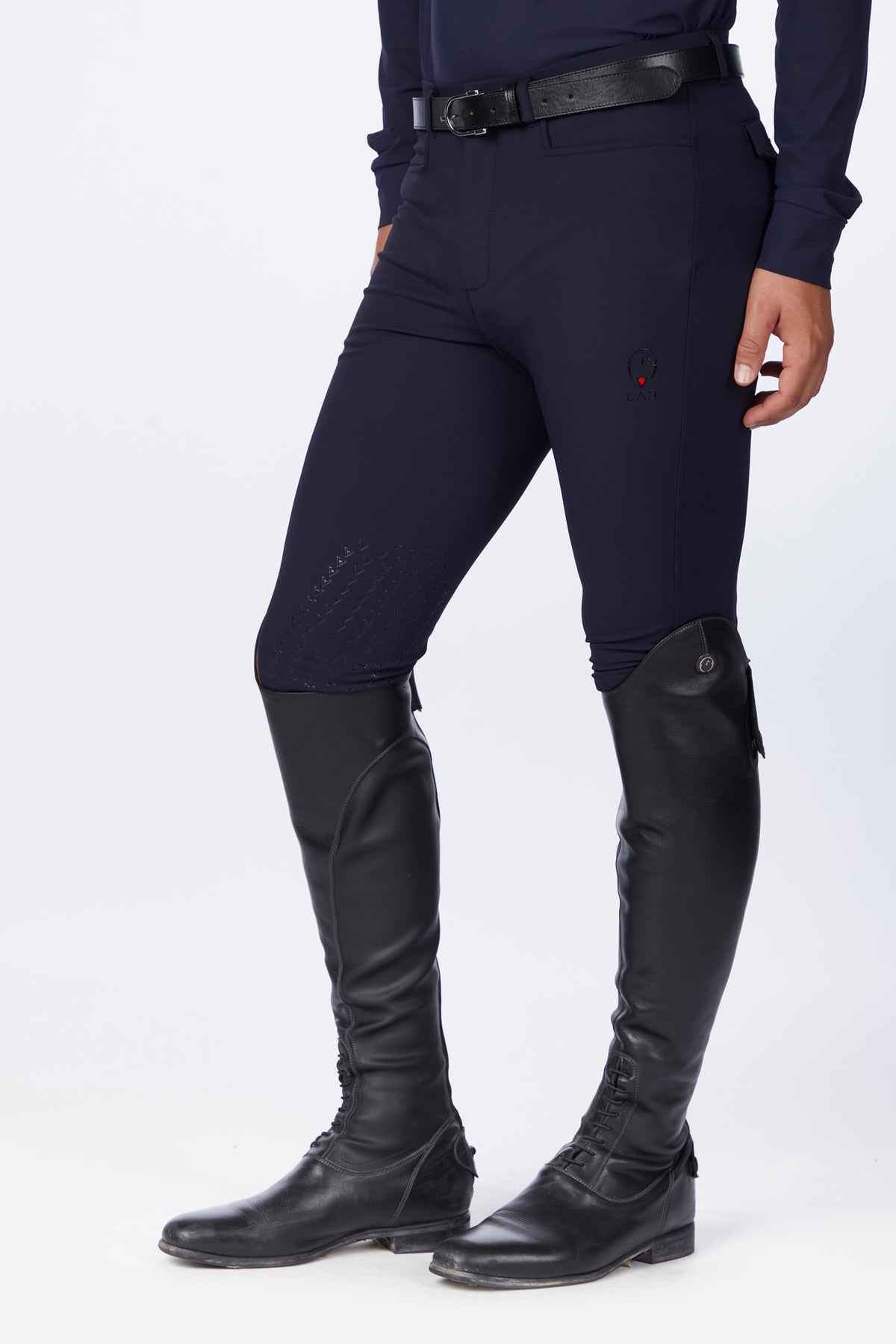 Person wearing navy riding pants and black riding boots on a white background