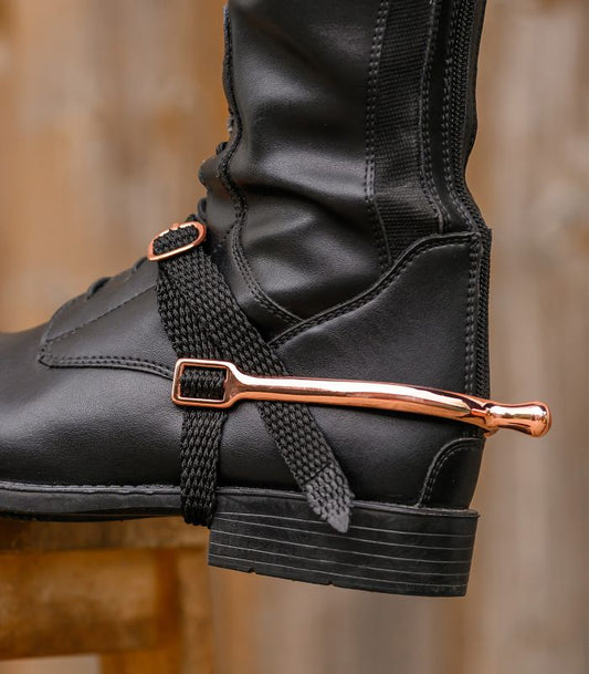 Black boot with a rose gold spur attached to the lace, on a blurred background