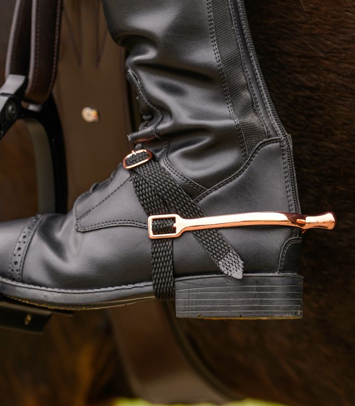 Black leather boot with a gold spur on a dark background