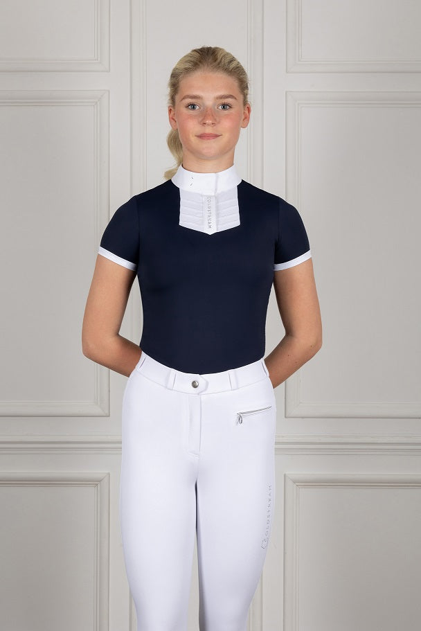 Person wearing a navy equestrian top with white collar and white pants against a neutral background