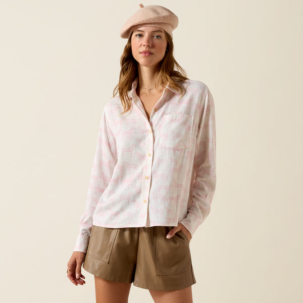 Woman wearing a light pink checkered shirt and beige shorts with a beige beret on a beige background