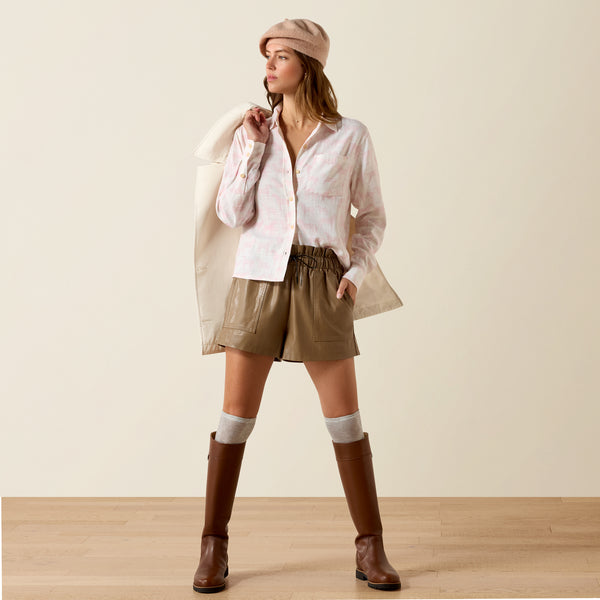 Woman wearing a white shirt, beige shorts, brown boots, and a beige hat on a plain background
