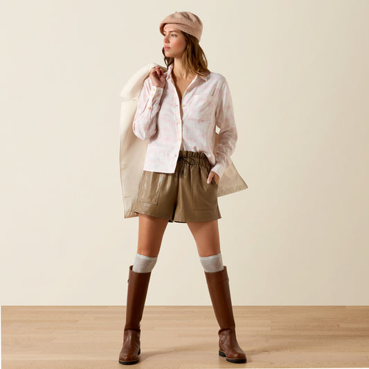 Woman wearing a white shirt, beige shorts, brown boots, and a beige hat on a plain background