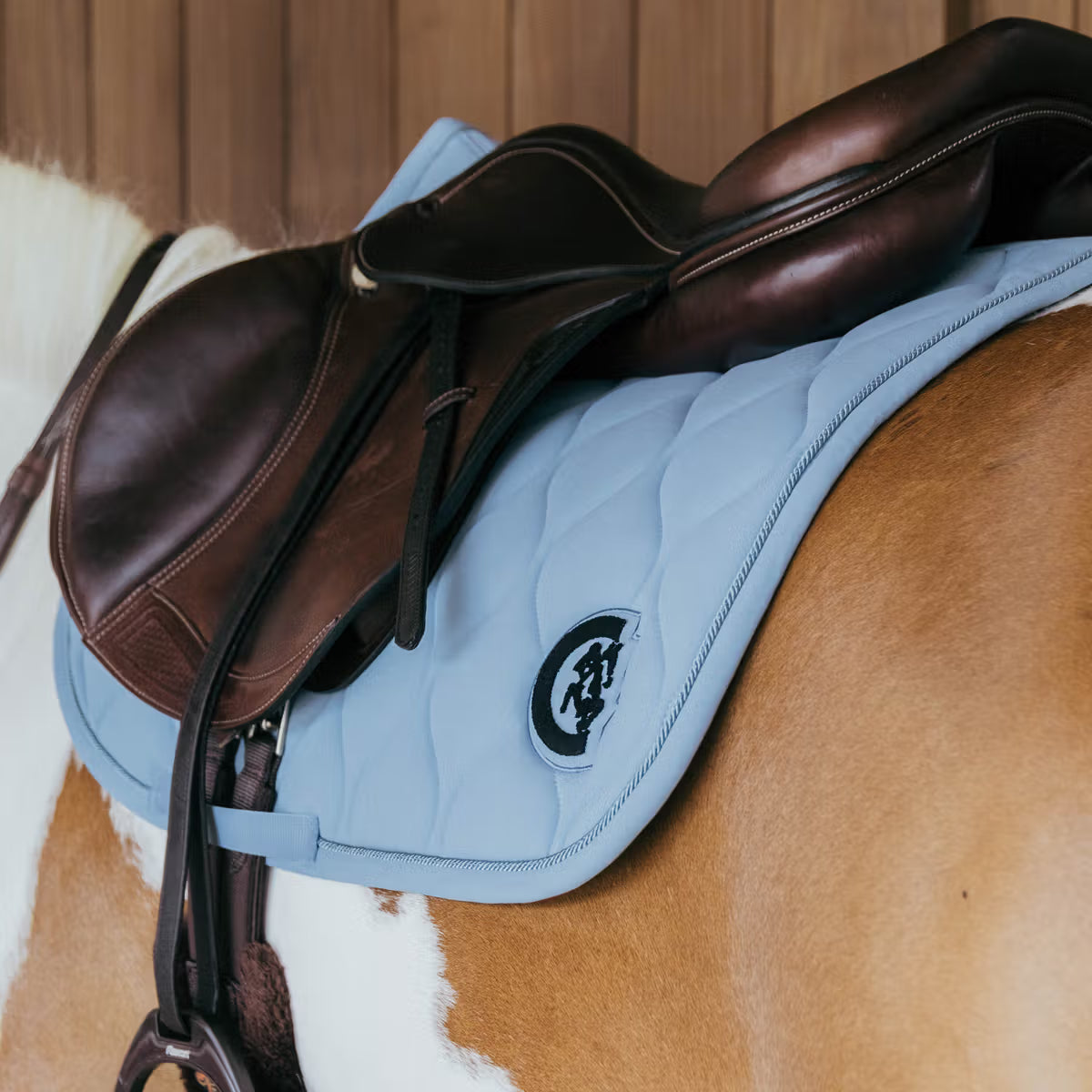 Brown saddle on a horse with a blue pad and visible brand logo.