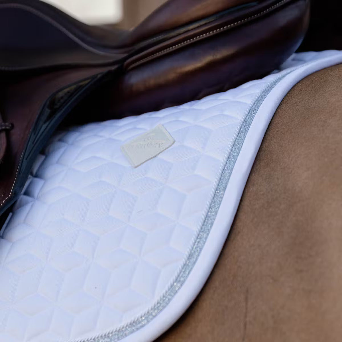 Close-up of a horse saddle with a quilted blue pad and brown leather saddle blanket.