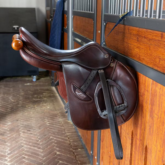 Brown leather saddle on a wooden wall in a stable.