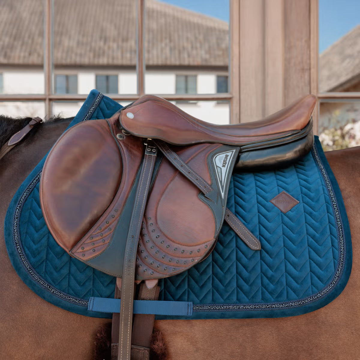 Brown saddle on a horse with a blue pad in an outdoor setting