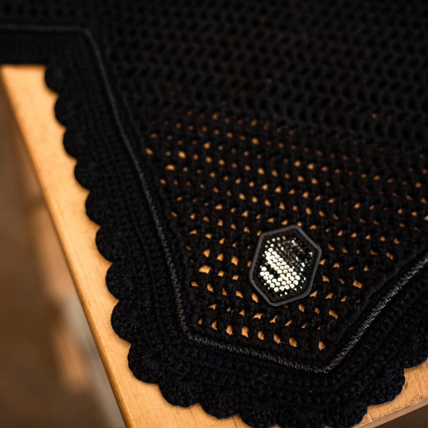 Close-up of a black textured fly veil  with a silver emblem on a wooden surface.