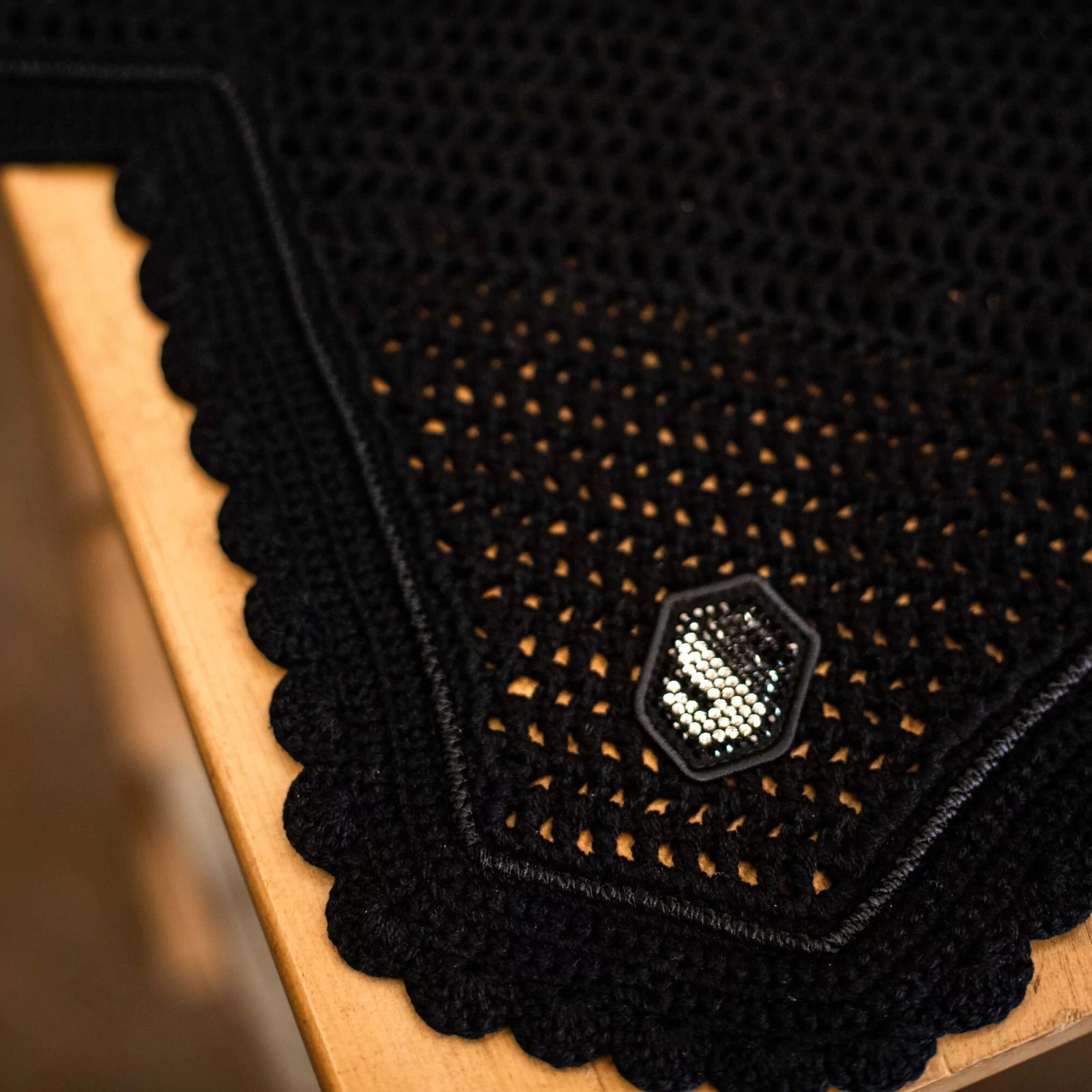 Close-up of a black textured fly veil  with a silver emblem on a wooden surface.