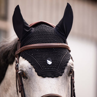 Horse wearing a black mesh fly mask with brown straps on a blurred background