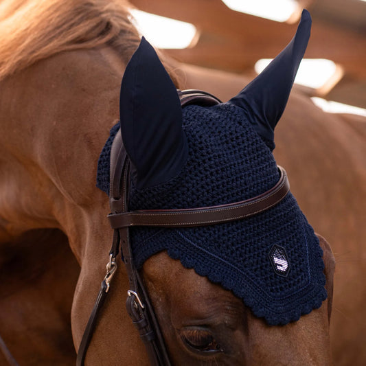 Horse wearing a dark blue fly mask with a logo on a blurred background