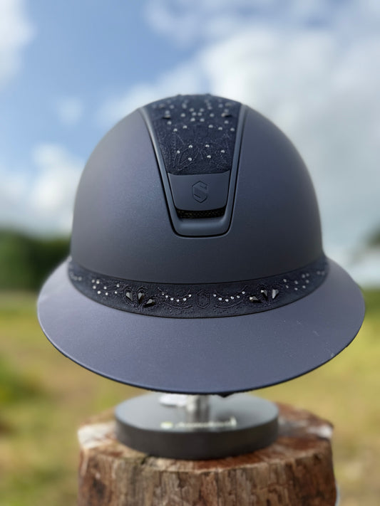Navy riding helmet with a logo on a wooden block against a blurred natural background