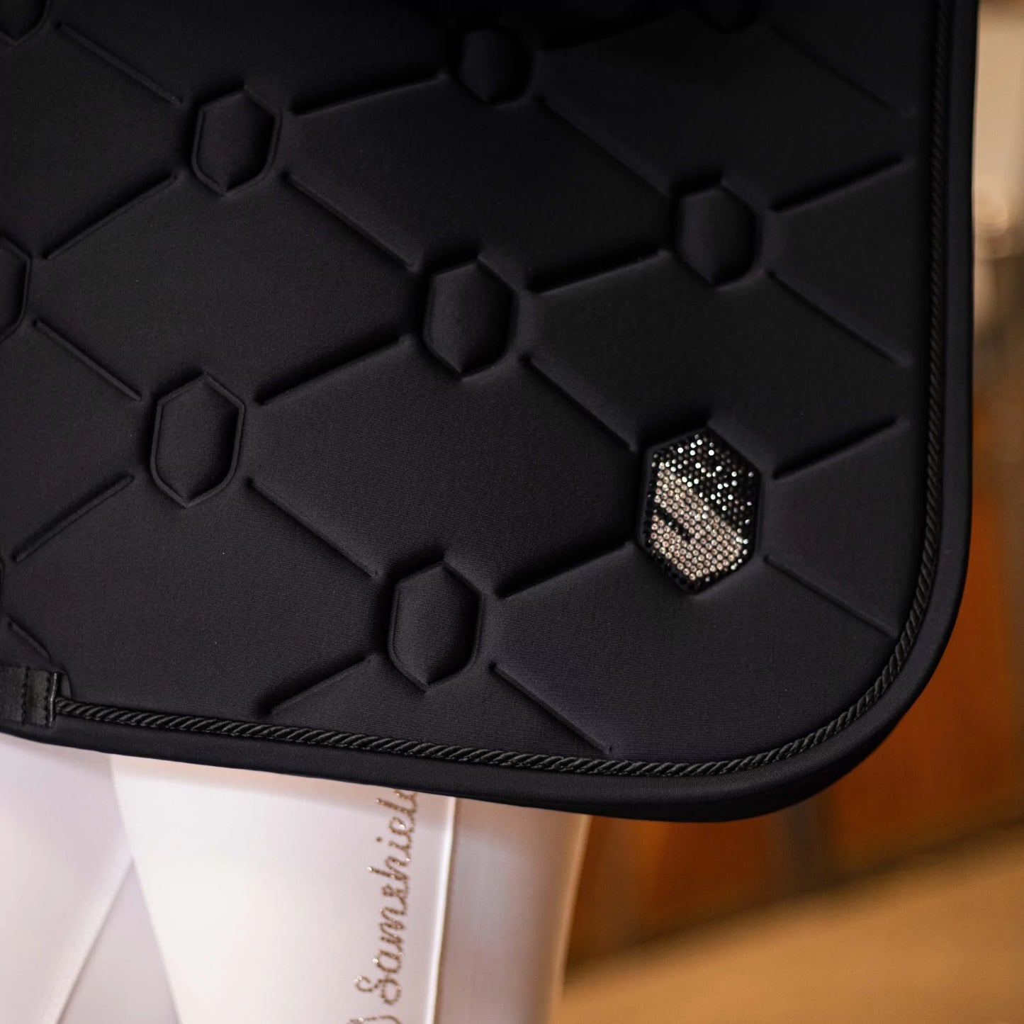 Black textured saddle pad with a diamond-like embellishment on a blurred background