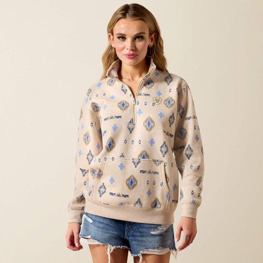Woman wearing a patterned beige pullover with denim shorts on a plain background