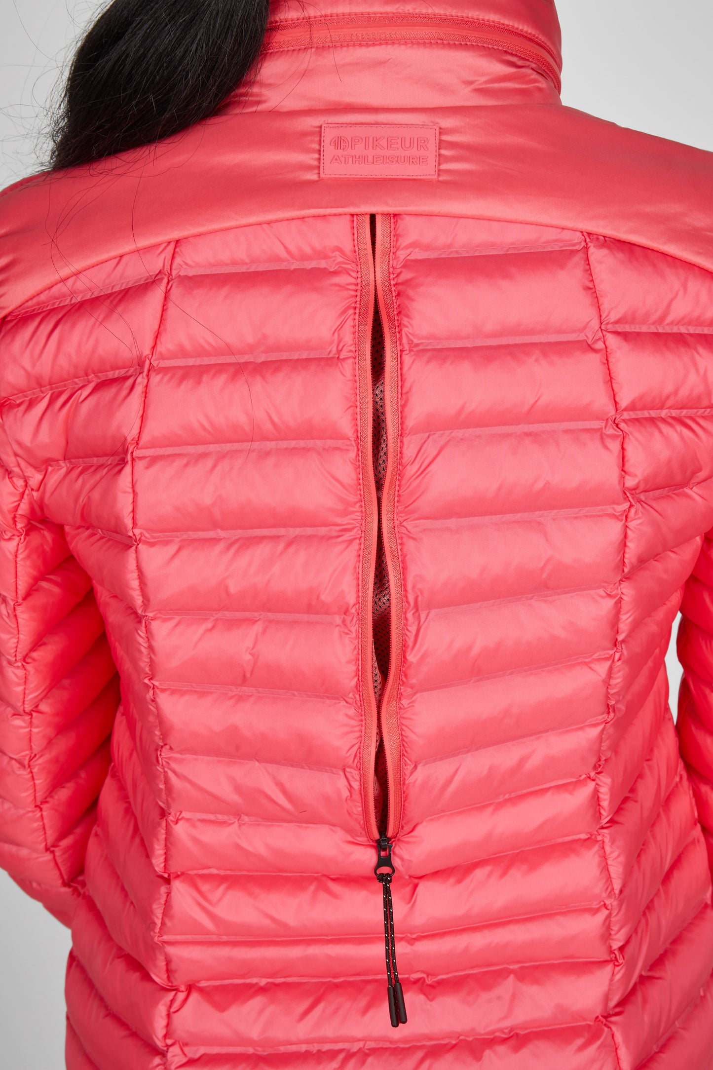 Close-up of a pink puffer jacket with a brand logo on a gray background