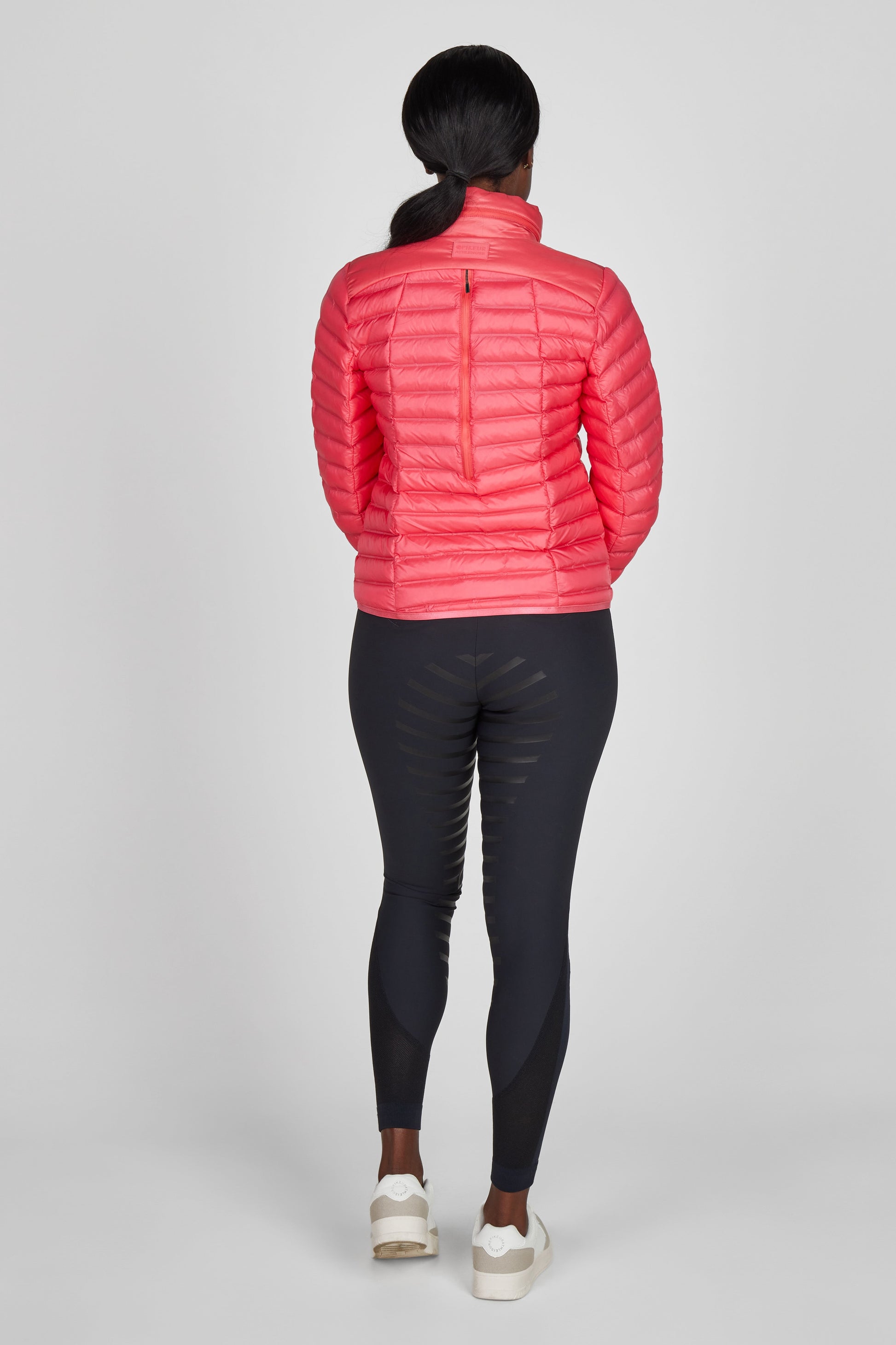 Person wearing a pink puffer jacket and black leggings on a white background