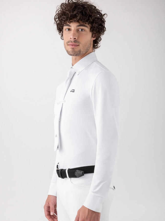 A man with curly dark hair wearing a white long-sleeve dress shirt, white tie, white trousers, and a black belt, photographed against a light gray studio background.
