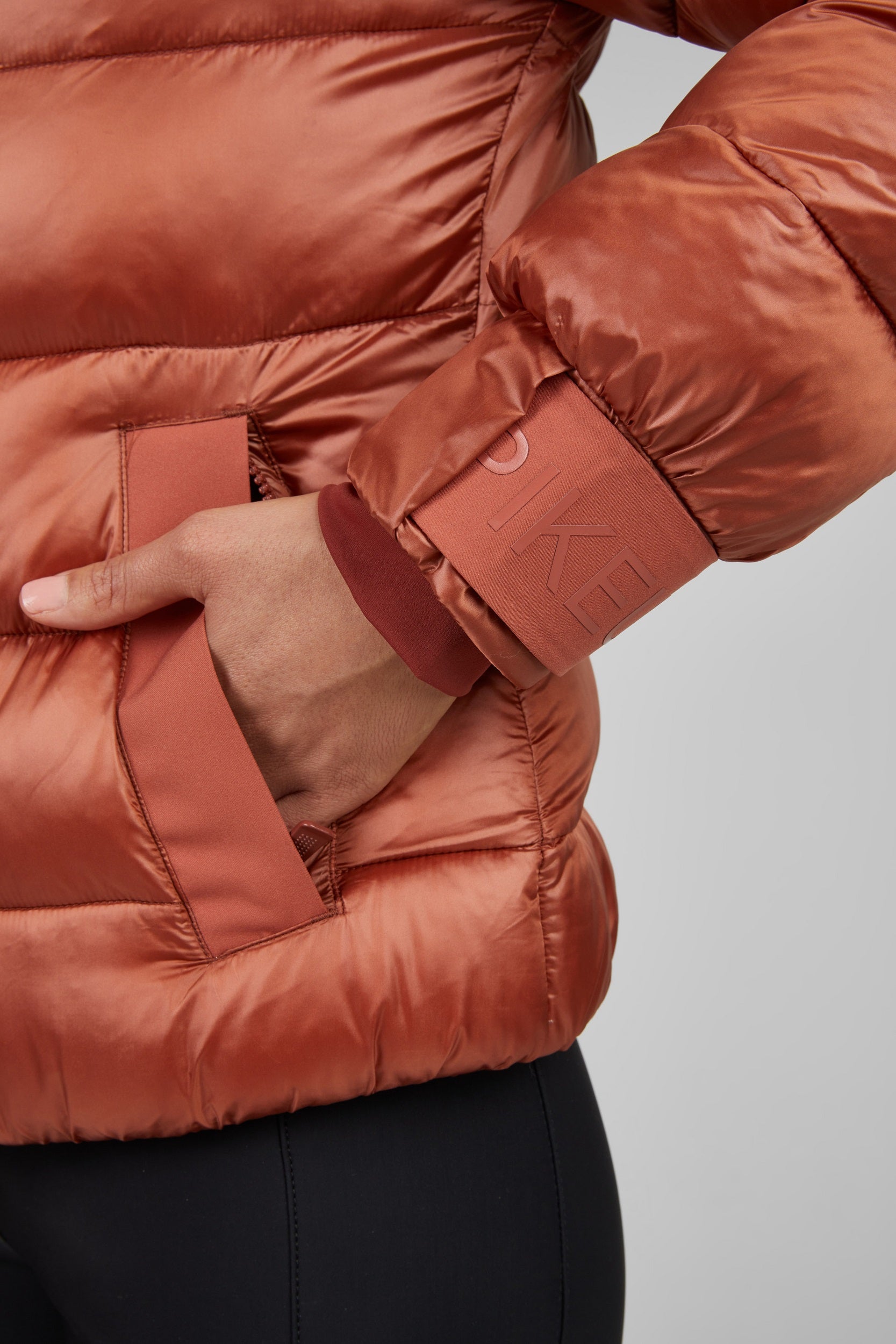 Close-up of a person wearing a rust-colored puffer jacket with a blurred background