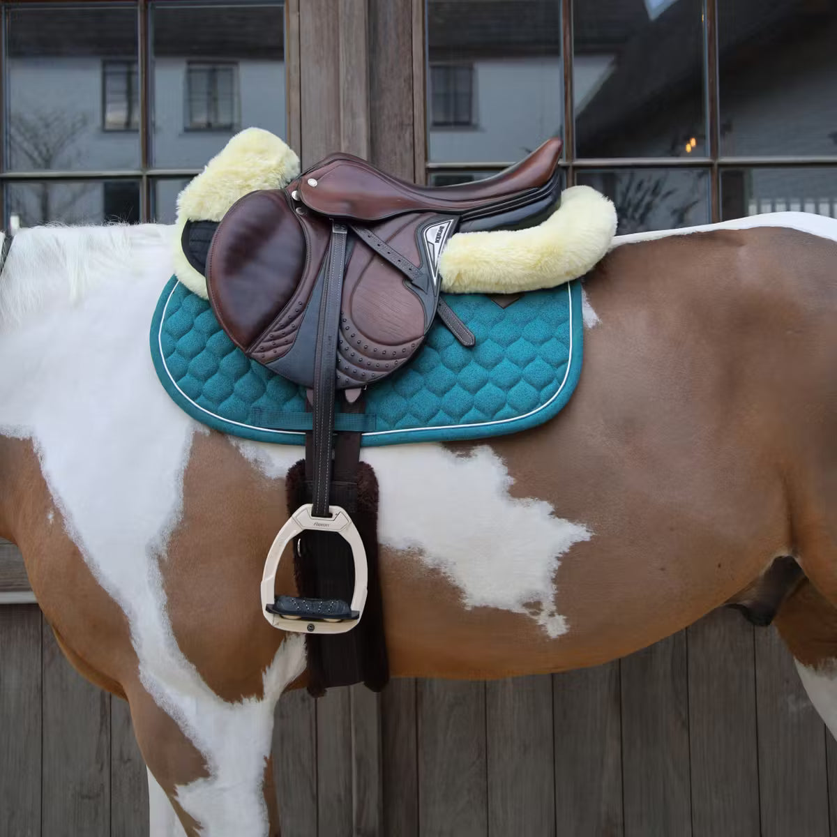 Horse with a brown saddle and blue pad on a wooden fence background