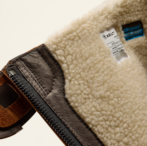 Close-up of a cream sherpa fleece lining with a brown leather zipper trim, showing a white Ariat brand tag and a blue OrShield waterproof label.