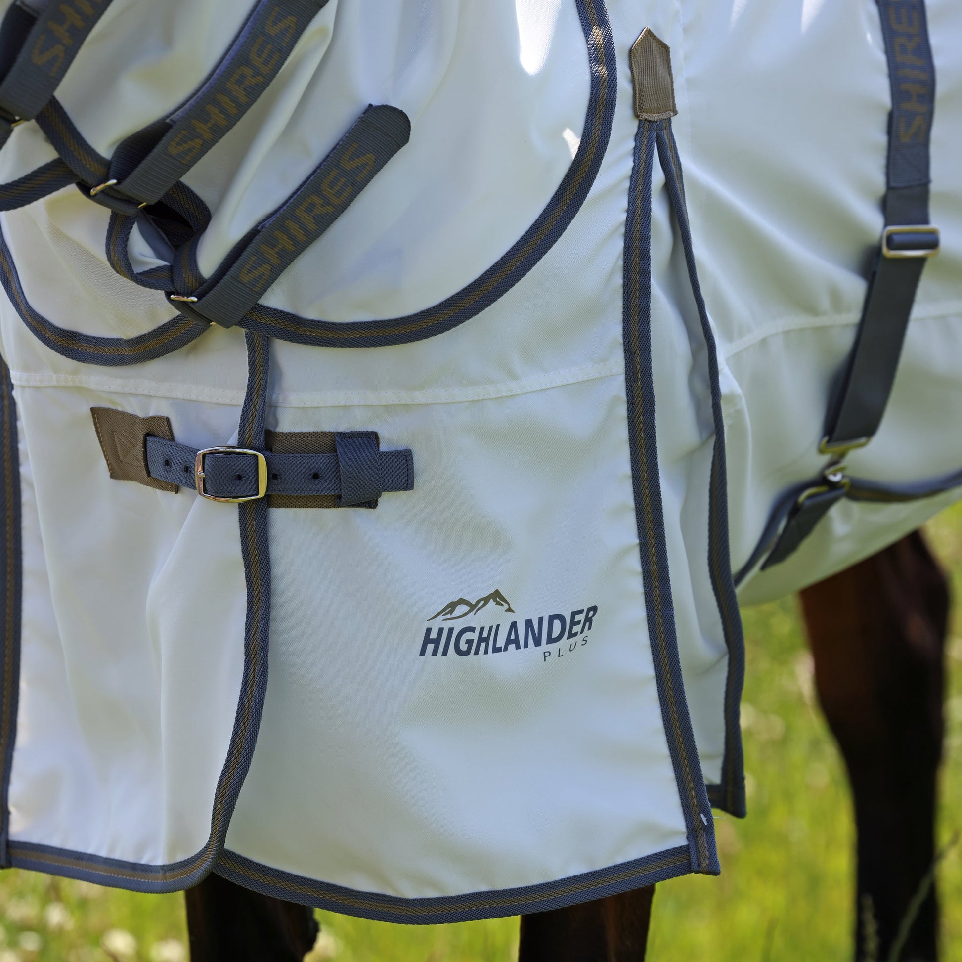 Close-up of a white horse blanket with 'Highlander' branding on a grassy background