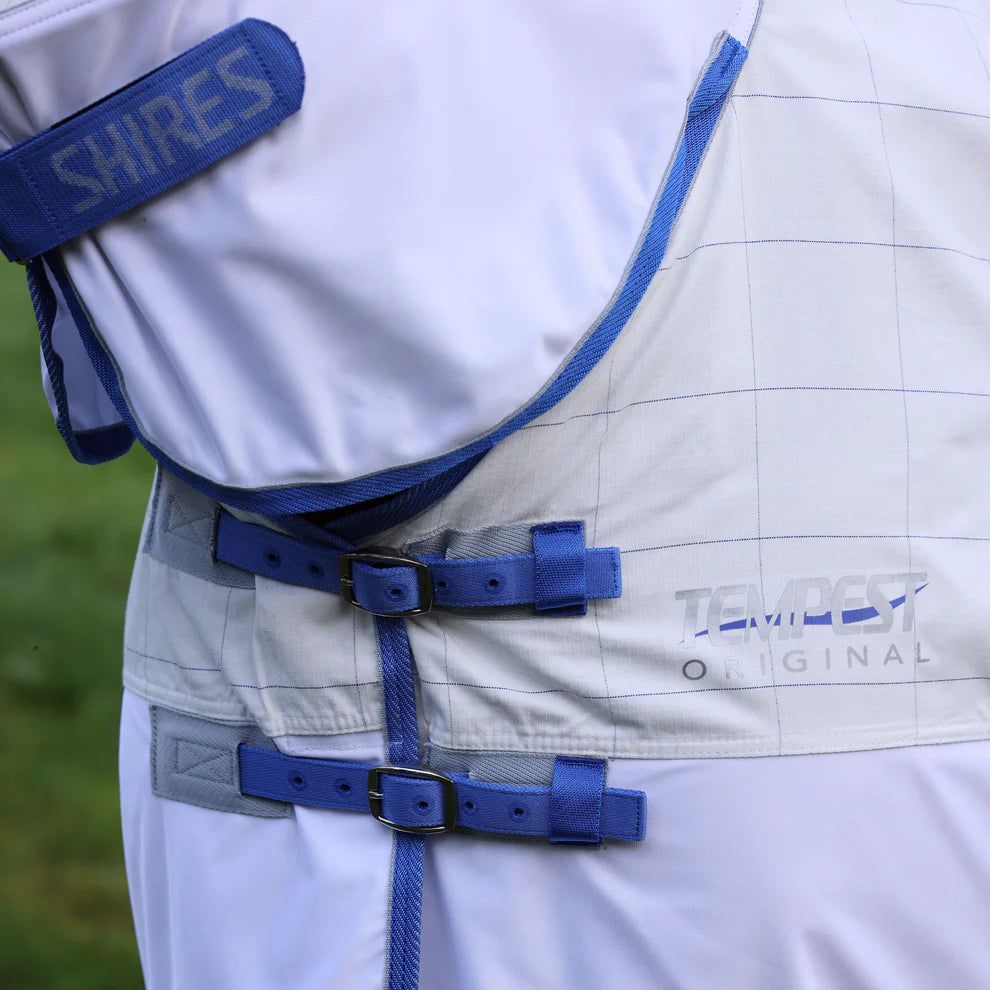 Close-up of a white equestrian blanket with blue straps and 'Shires' branding.