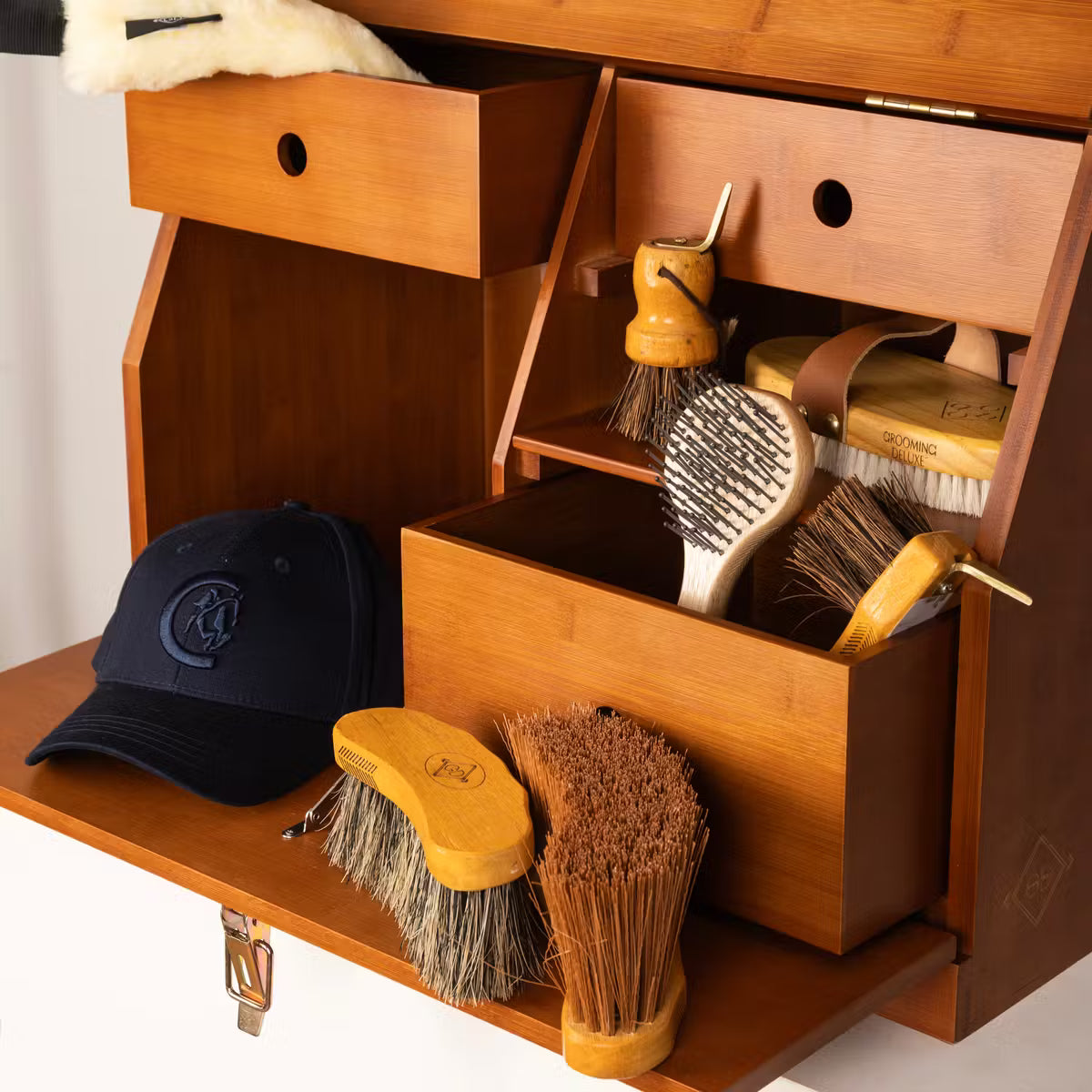 Wooden shoe shine cabinet with various brushes and a cap on a white background