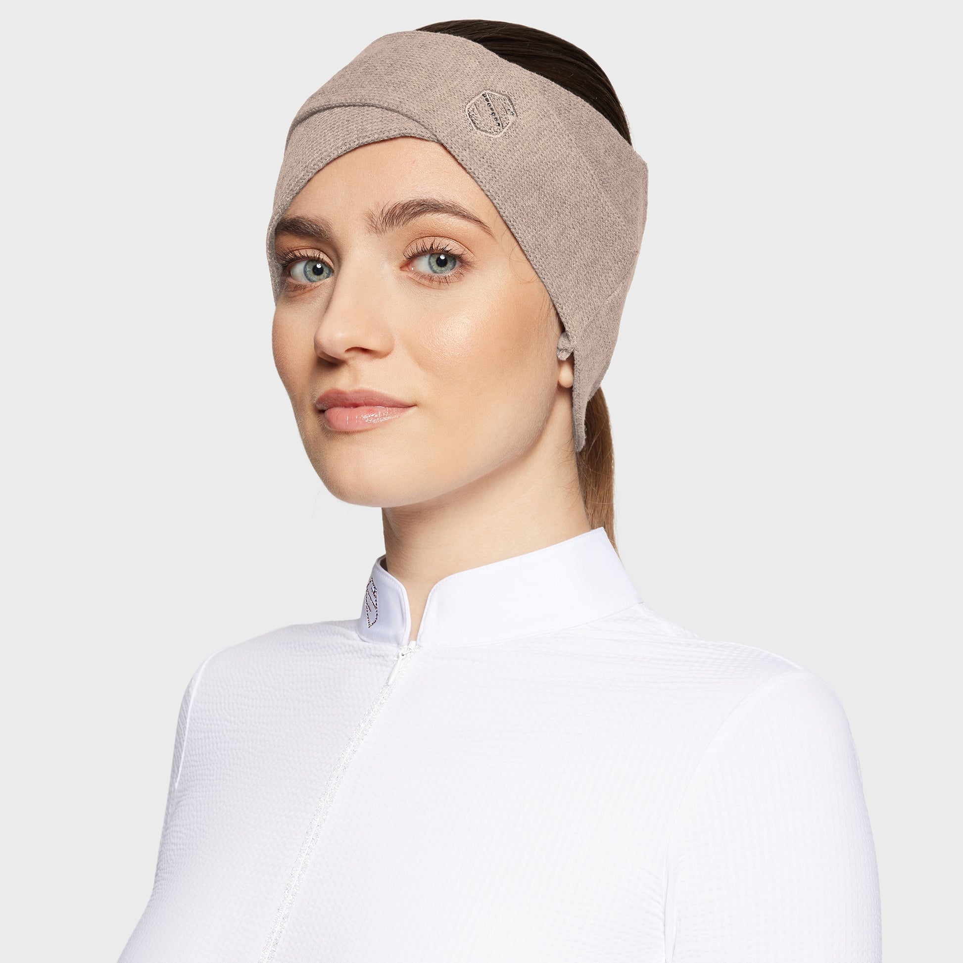 Woman wearing a beige criss cross headband with a white shirt on a white background
