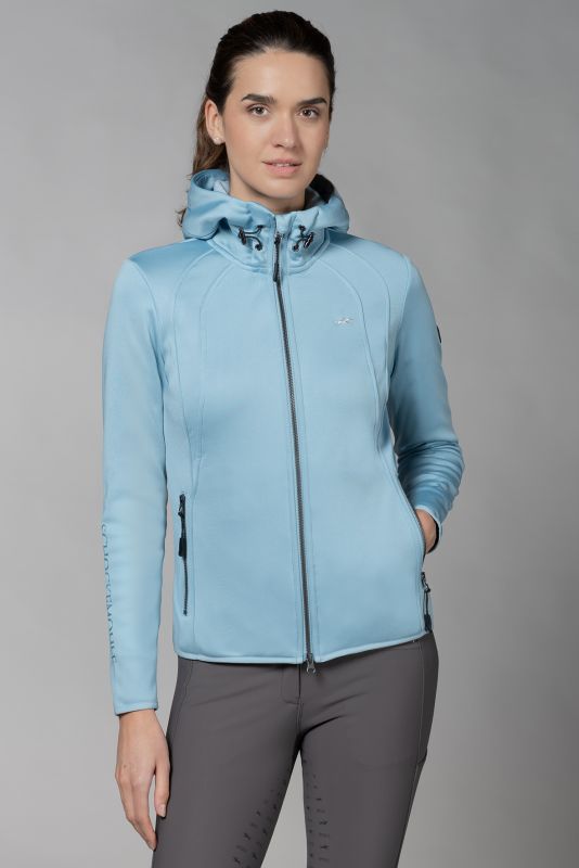 Woman wearing a blue sporty jacket and grey riding pants on a grey background