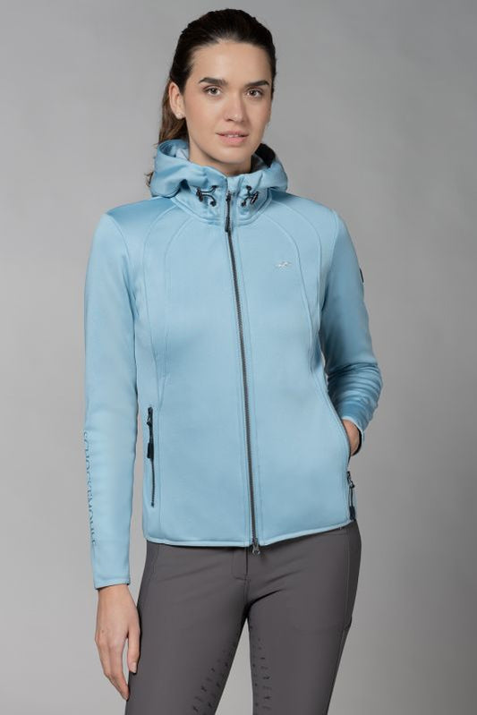 Woman wearing a blue sporty jacket and grey riding pants on a grey background