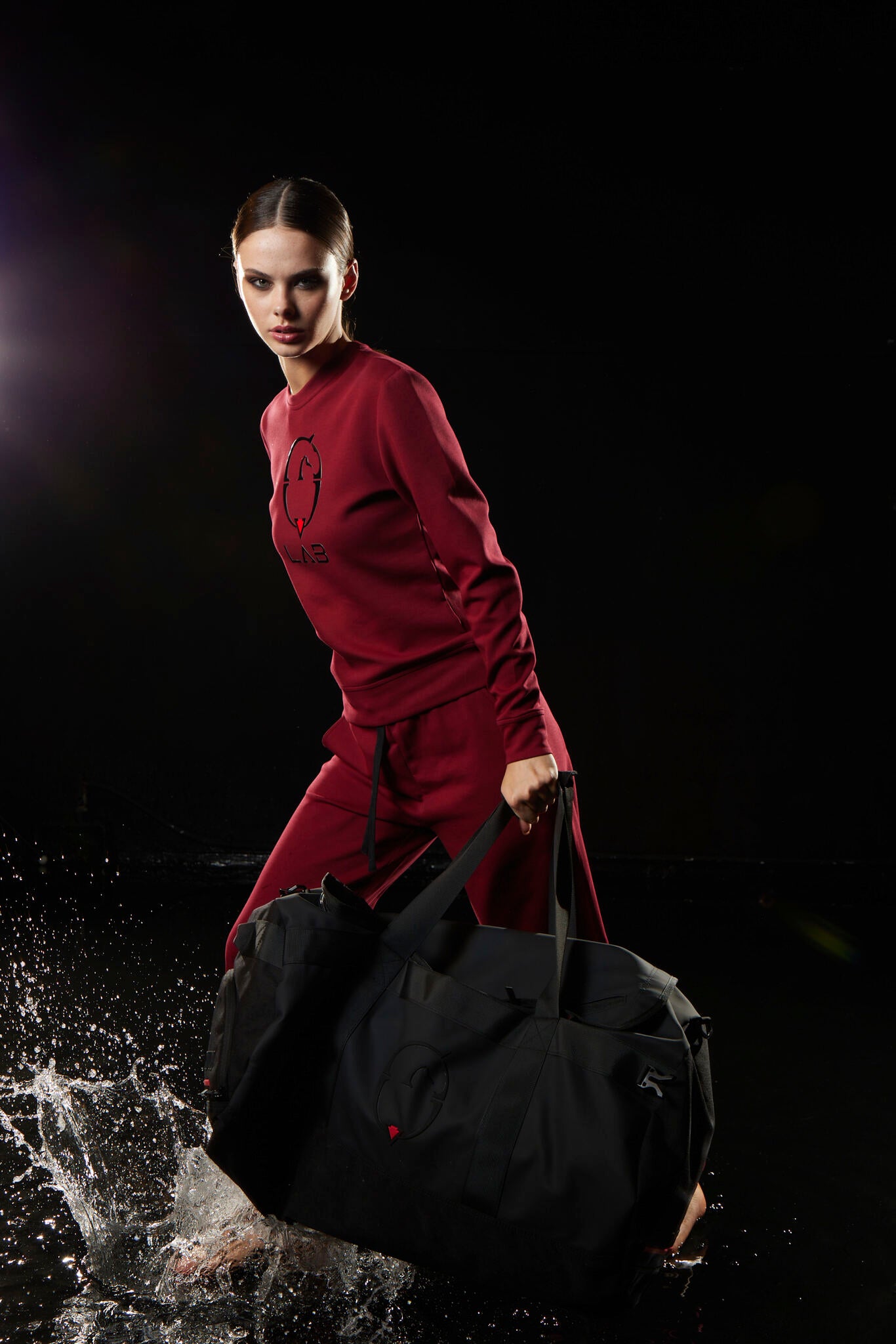 Person in a red outfit holding a black bag against a dark background