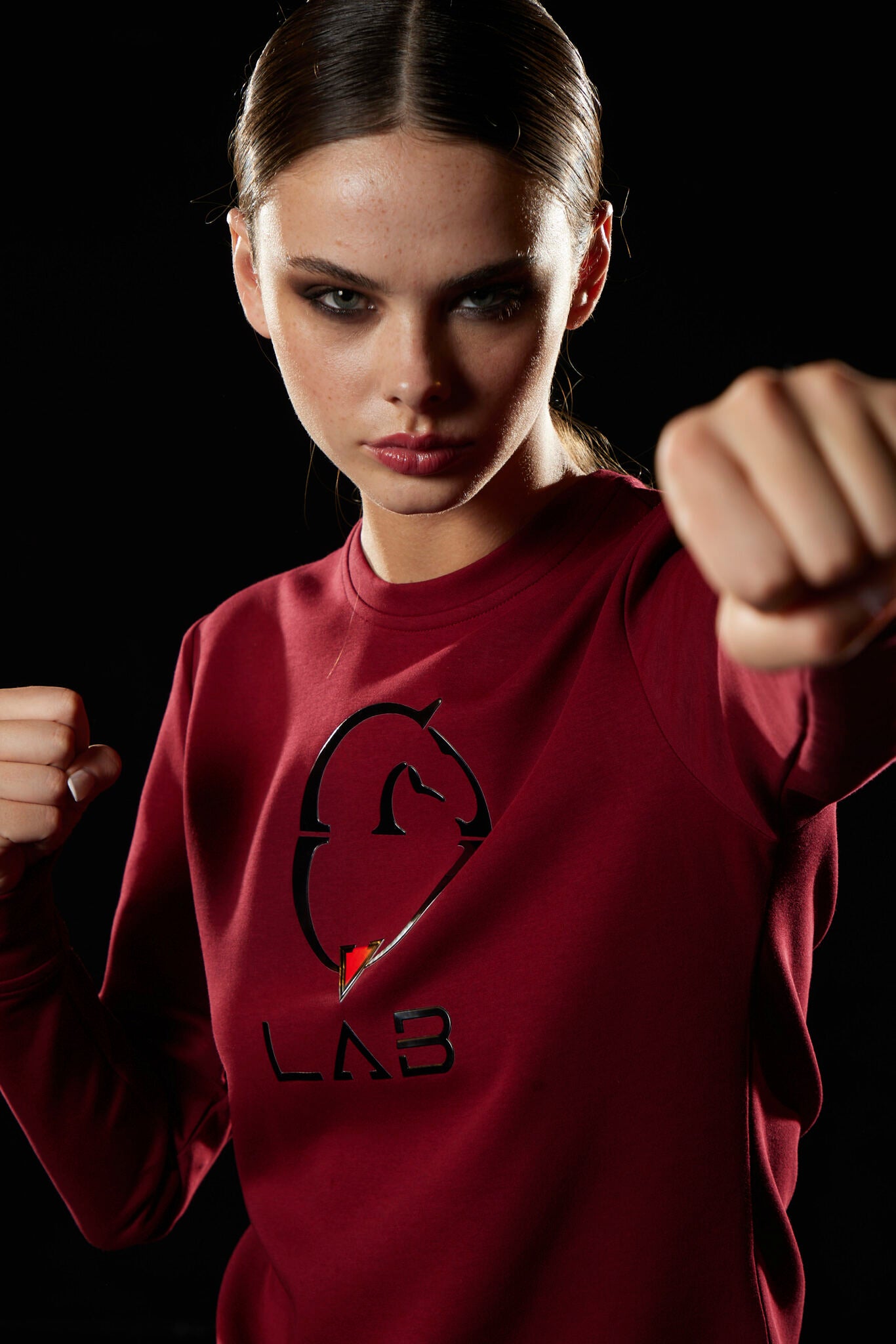 Woman wearing a red sweatshirt with a logo, posing against a black background