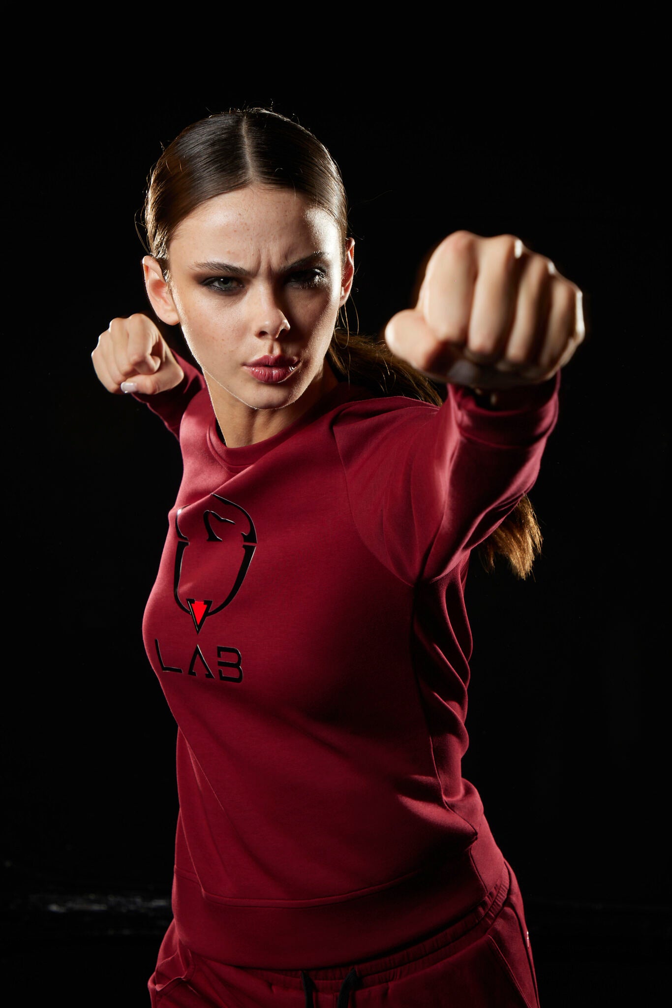 Person in red athletic wear with a logo, posing with fists outstretched on a black background