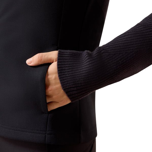 Close-up of a person wearing a navy ribbed long-sleeve top or jacket, with one hand reaching into a side pocket against a white background.