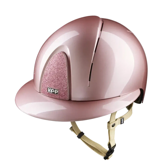 A metallic pink equestrian riding helmet with a glittery pink cheek protector and a beige chin strap, shown on a solid white background.