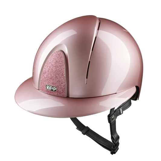 A shiny light pink equestrian riding helmet with a glittery pink cheek pad and a black chin strap, shown on a solid white background.