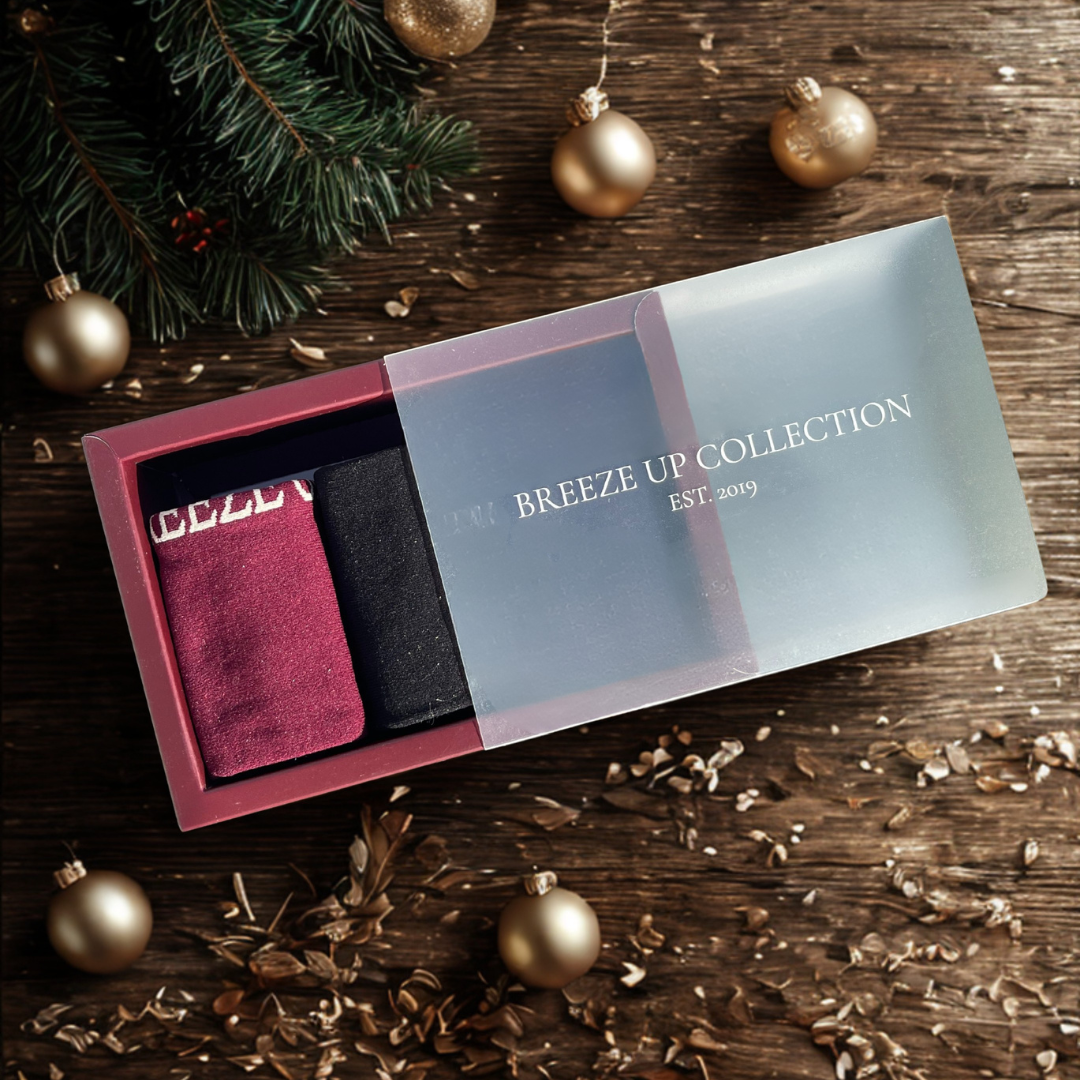 Three pairs of socks in a box labeled 'Breeze Up Collection' on a wooden surface with Christmas decorations.