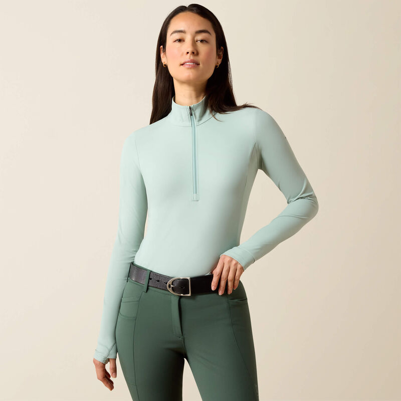 Woman wearing a light blue long-sleeve top and green pants against a beige background