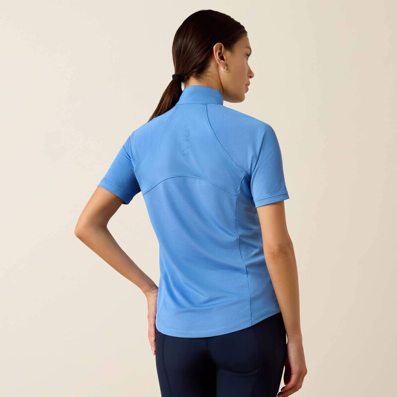 Woman wearing a blue athletic shirt and dark pants on a beige background