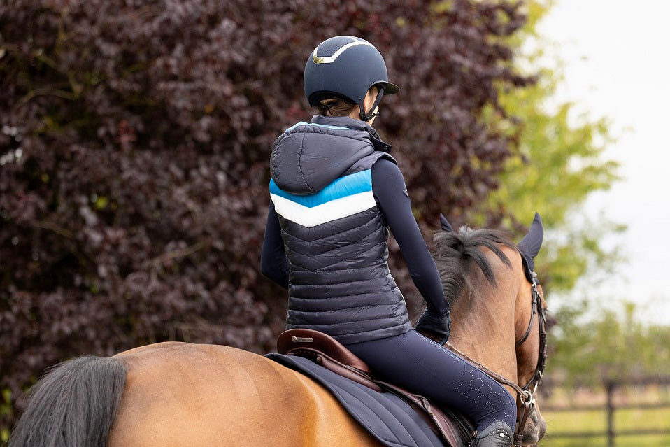 Person riding a horse wearing a helmet and equestrian attire in an outdoor setting.