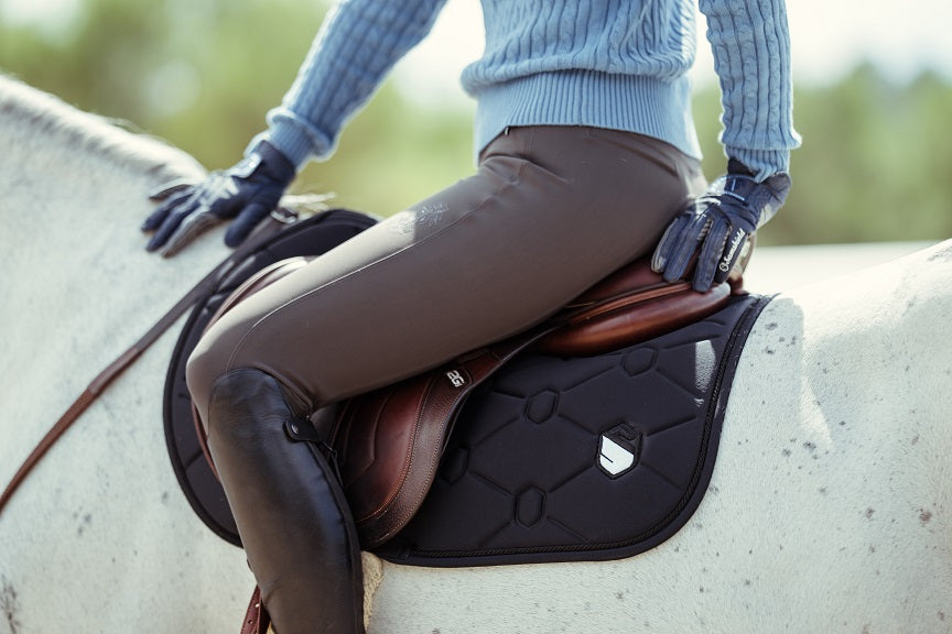 Person sitting on a horse wearing a brown saddle, grey pad and gloves.
