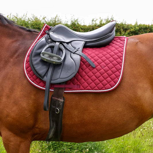 Horse wearing a gray saddle and red quilted saddle pad in a grassy field.