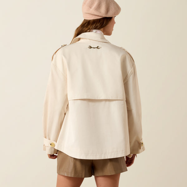 Person wearing a beige coat and shorts with a matching hat on a plain background