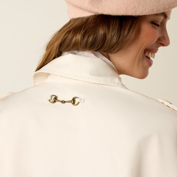 Woman wearing a cream-colored coat with a gold buckle detail on a plain background
