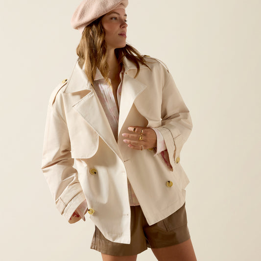 Woman wearing a beige trench coat and beret on a plain background