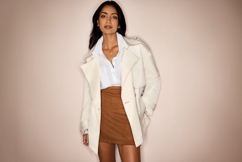 Woman wearing a white coat over a white shirt and brown skirt on a beige background