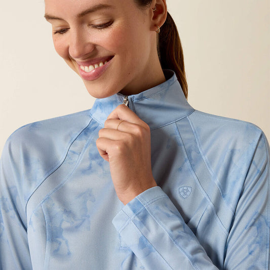 Woman wearing a light blue patterned shirt with a visible brand logo on a beige background